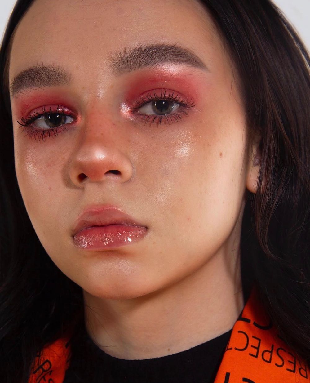 Close-up of a young woman wearing bold red smoky eye makeup with glossy lips and dramatic lashes.