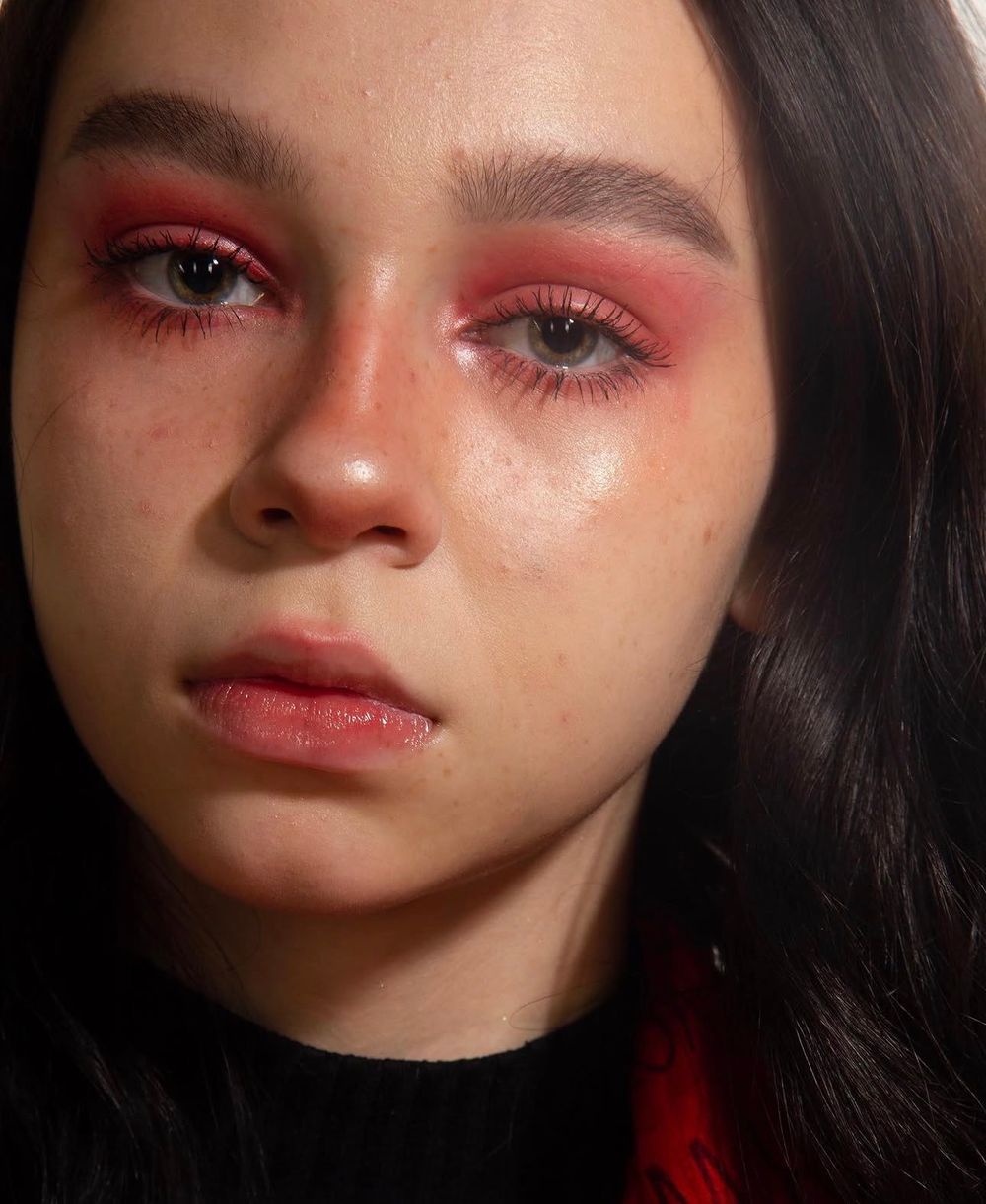 Close-up of a young woman with dramatic red eye makeup, dark lashes, and natural dewy skin.
