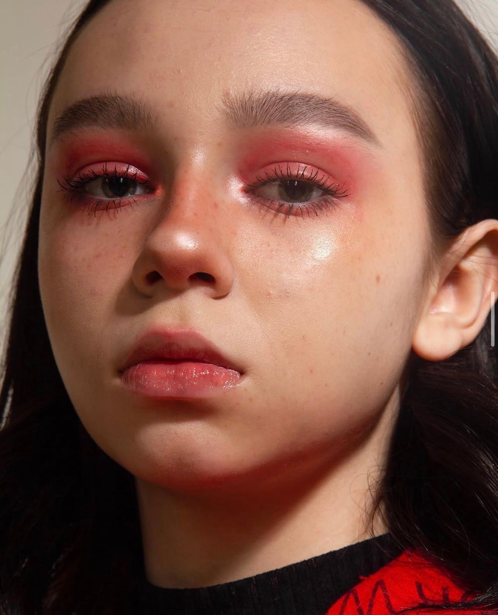 Close-up portrait of a young woman with striking red eyeshadow makeup and natural glowing skin.