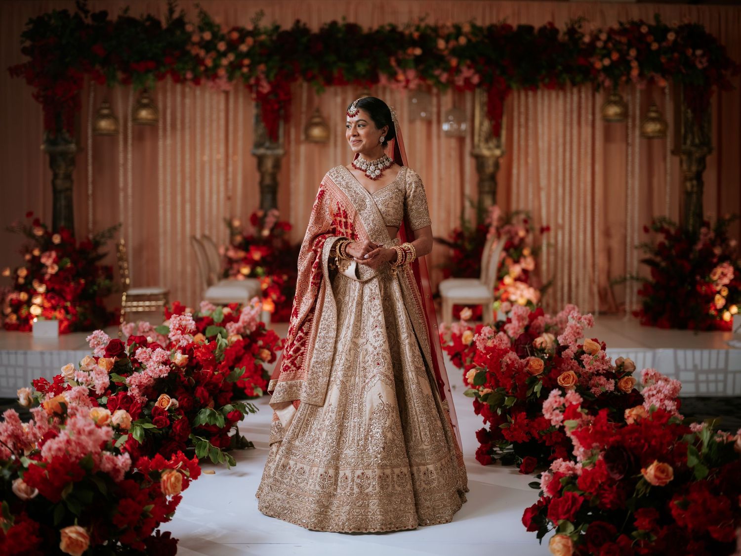 An elegant Indian bride poses on a floral mandap at Hilton Pearl River, NY, showcasing bridal fashion and luxury wedding décor.