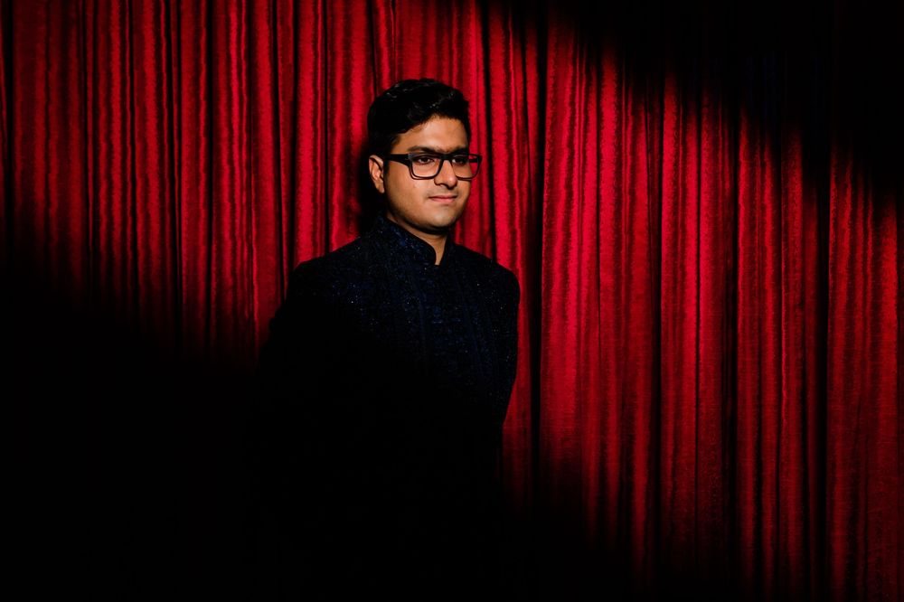 Person in black outfit poses against a dramatic red curtain backdrop in a theatrical portrait photo.