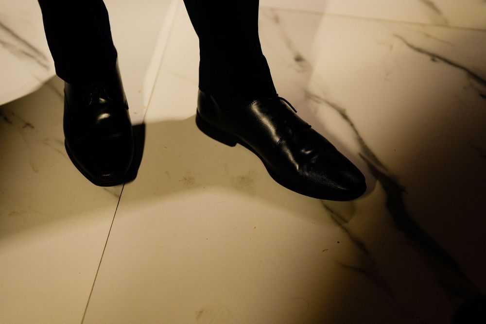 Close-up of polished black leather loafer shoes on a marble floor with dramatic shadows.