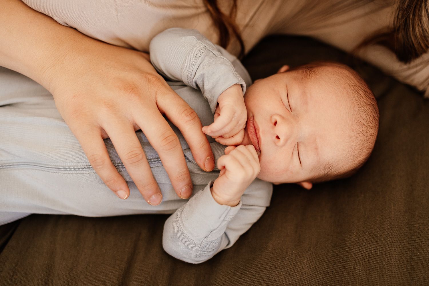 a newborn baby lays on the bed with mom's hand on his tummy while he sleeps