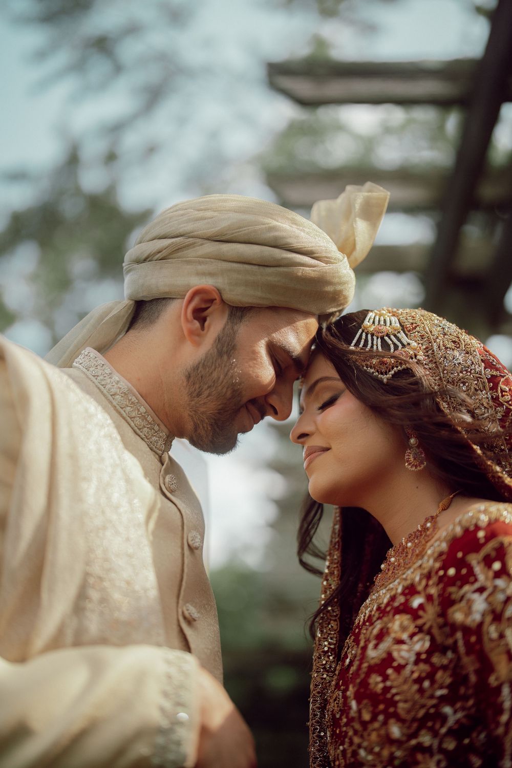 South Asian bride and groom in traditional wedding attire touching foreheads in an intimate romantic moment.