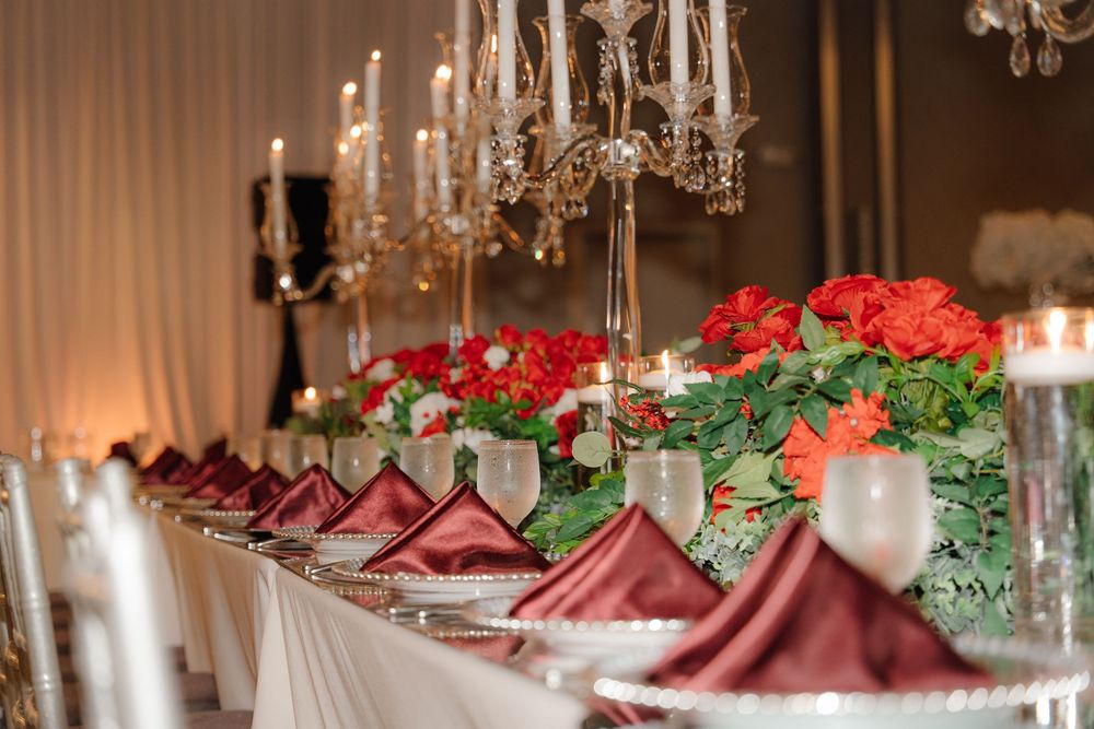 Elegant banquet table with red roses, crystal chandeliers, and burgundy napkins for a formal wedding reception.