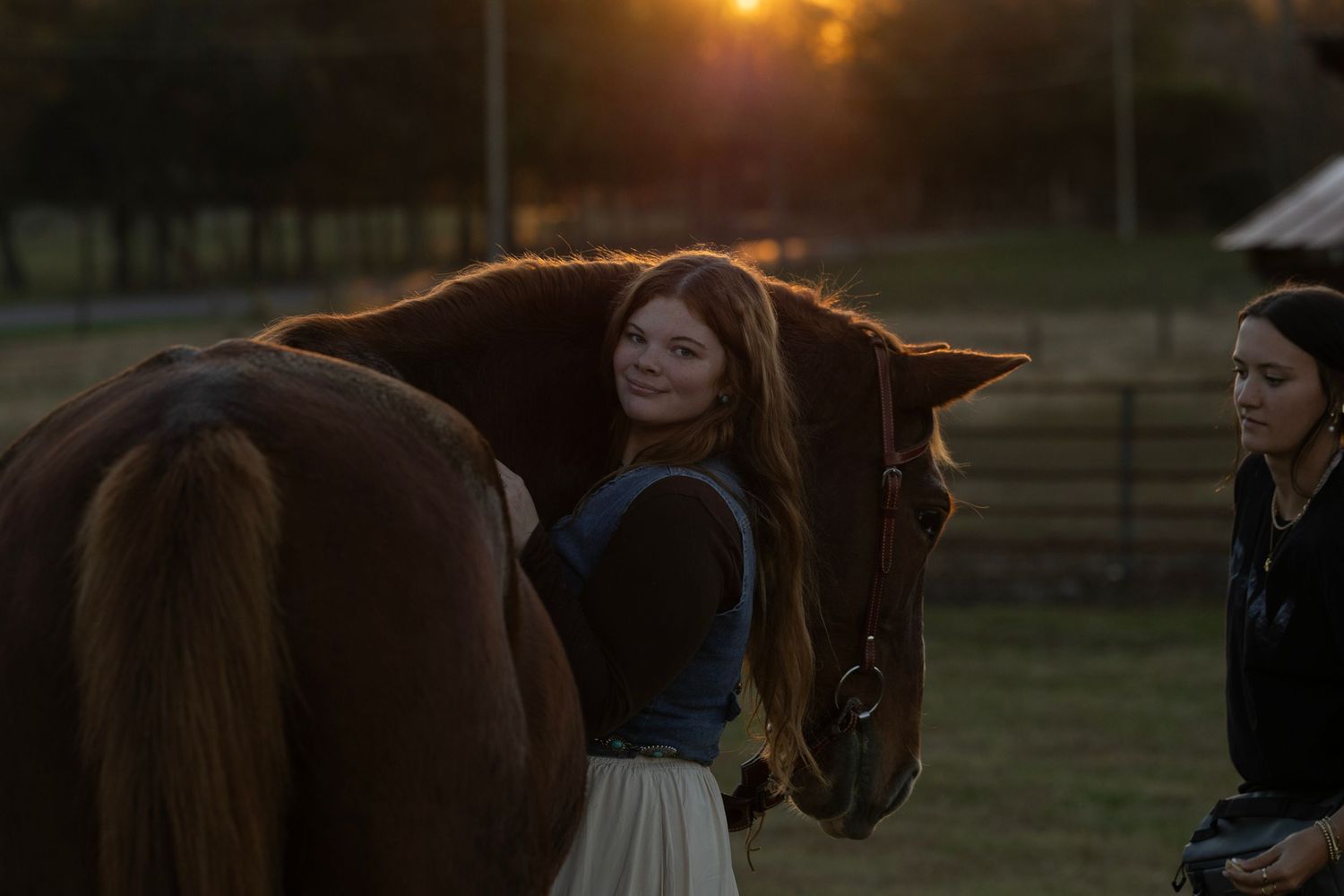 Woman smiling while embracing a brown horse at golden hour sunset on a ranch.