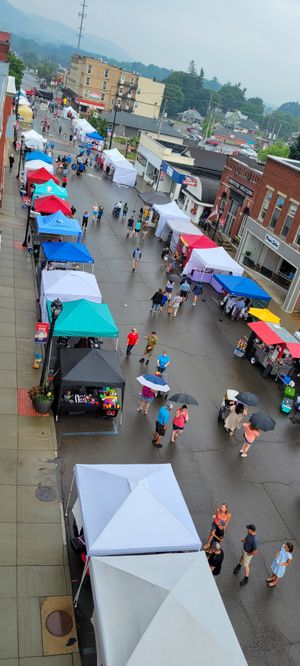 Aerial view of a colorful outdoor street festival with vendor tents lining a busy downtown street on a cloudy day.