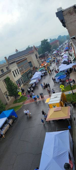 Aerial view of a rainy outdoor street festival with colorful vendor tents lining a wet downtown street.