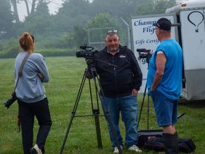 Three people filming outdoors near a Champagne Flights gift certificate trailer on a foggy day.