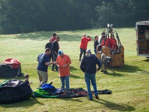 Group of people preparing a hot air balloon for launch on a sunny green field with trees in the background.
