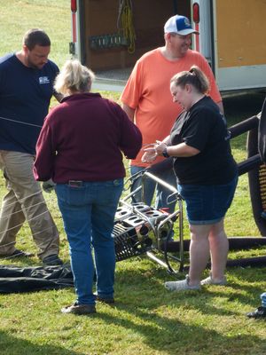 Four people assembling equipment outdoors near a trailer on green grass, working together on a metal frame structure.