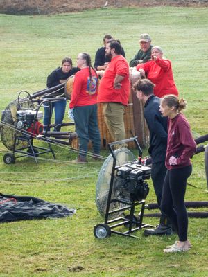 Group of people in red shirts prepare equipment and generators on a green lawn.