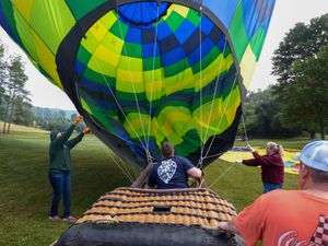People inflating a colorful green and blue hot air balloon on a grassy field, with crew members guiding the envelope.