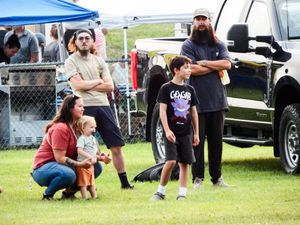 Families gather outdoors at a community event near trucks and tents on a green lawn.