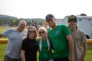 Group of five people posing together outdoors at a summer event, wearing casual clothes including green shirts.