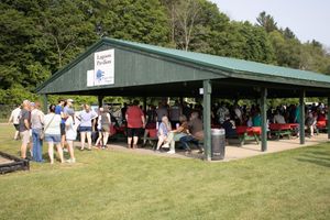 Outdoor picnic pavilion filled with guests enjoying a sunny day in a lush green park setting.