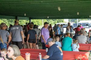 Large crowd gathered under a pavilion at an outdoor community picnic event on a summer day.