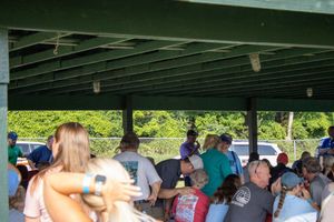 Group of people socializing under a green covered outdoor pavilion during a casual community gathering event.