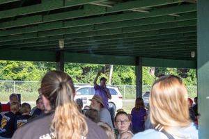 Group of people gathered under a green pavilion shelter at an outdoor event on a sunny day.