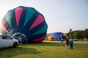 Colorful hot air balloons being inflated on a green field at a balloon festival on a clear summer day.