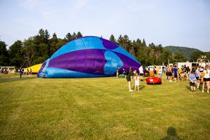 A colorful hot air balloon being inflated on a green field with spectators watching at an outdoor festival.
