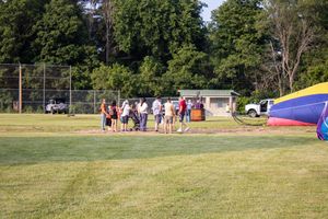 Group of people gathered on a green field near a colorful hot air balloon being inflated outdoors.