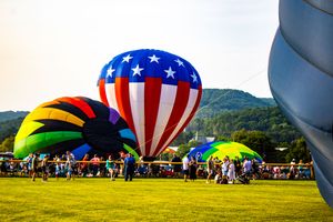 Colorful hot air balloons including a patriotic American flag design inflate at an outdoor festival on a green field.