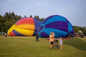 Colorful hot air balloons being inflated on green grass field with family and stroller at outdoor balloon festival.