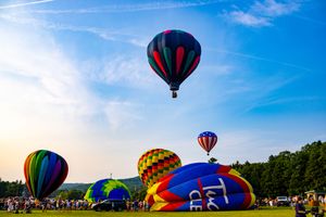 Colorful hot air balloons launching and flying at an outdoor festival on a sunny day with blue skies.