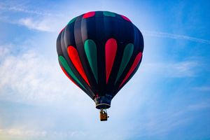 A dark blue hot air balloon with red and green panels soaring against a bright blue sky.