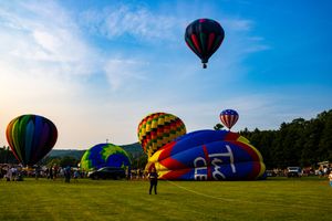 Colorful hot air balloons launching at a festival on a green field under a bright blue sky at sunset.