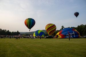 Colorful hot air balloons launching and flying over a green field at a balloon festival on a clear morning.
