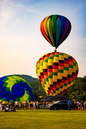 Colorful hot air balloons launching at a festival on a sunny day with crowds gathered on green grass.