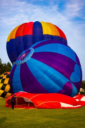 Colorful hot air balloons being inflated on green grass at a balloon festival under a blue sky.