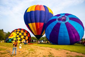 Colorful hot air balloons inflating on a green field at a balloon festival under a clear blue sky.