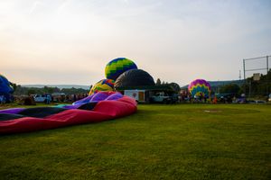 Colorful hot air balloons being inflated on a green field at dusk during an outdoor balloon festival.
