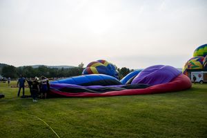 Hot air balloons being inflated on a green field at dawn during a balloon festival.