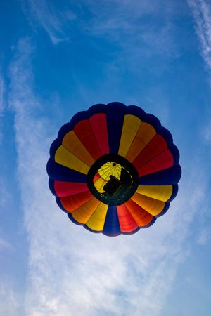 Colorful hot air balloon with red, yellow, and blue panels soaring against a bright blue sky, viewed from below.