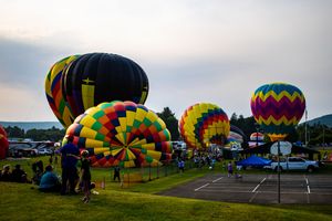 Colorful hot air balloons inflating at dusk during an outdoor balloon festival on a green field.