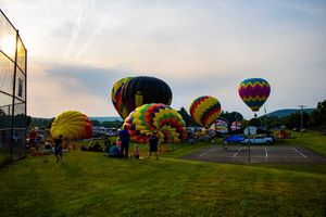 Colorful hot air balloons inflating at dusk during an outdoor balloon festival on a green field.