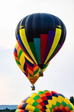 Colorful hot air balloons soaring in the sky at a balloon festival, featuring vibrant rainbow patterns against a cloudy backdrop.