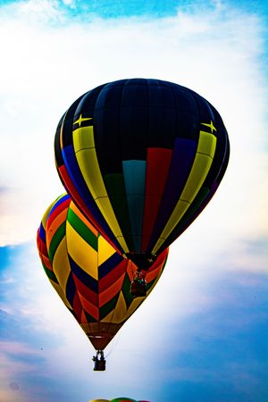 Two colorful hot air balloons soaring against a blue sky, featuring vibrant stripes in red, yellow, green, and blue patterns.
