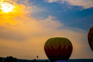 Hot air balloons float at sunrise with vibrant golden sky and blue clouds in a scenic outdoor festival setting.