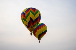Two colorful hot air balloons with zigzag patterns soar against a pale sky.