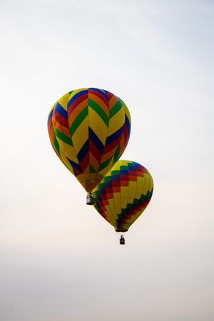 Two colorful hot air balloons with rainbow chevron patterns floating in a hazy sky.