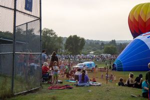 Crowd gathers on grass field near colorful hot air balloon at outdoor festival during evening.
