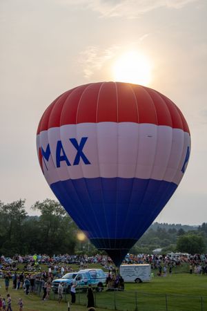 RE/MAX hot air balloon inflated at sunset during an outdoor festival, surrounded by crowds on a green field.