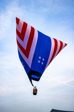 Patriotic American flag hot air balloon with red, white, and blue stripes and stars soaring against a blue sky.