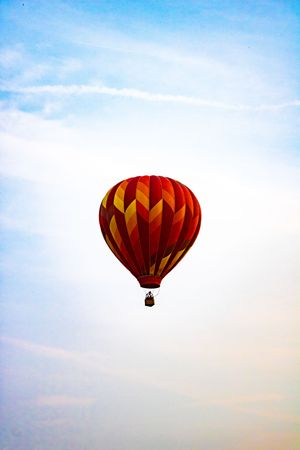A vibrant red and yellow striped hot air balloon soaring against a soft blue sky with wispy clouds.
