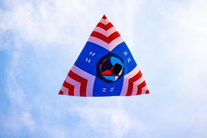 Colorful triangular kite with red, white, and blue stripes and a peace symbol flying against a cloudy sky.